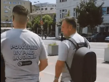 Dvaja členovia tímu v tričkách „Powered by paid invoices“ na ulici v Bratislave